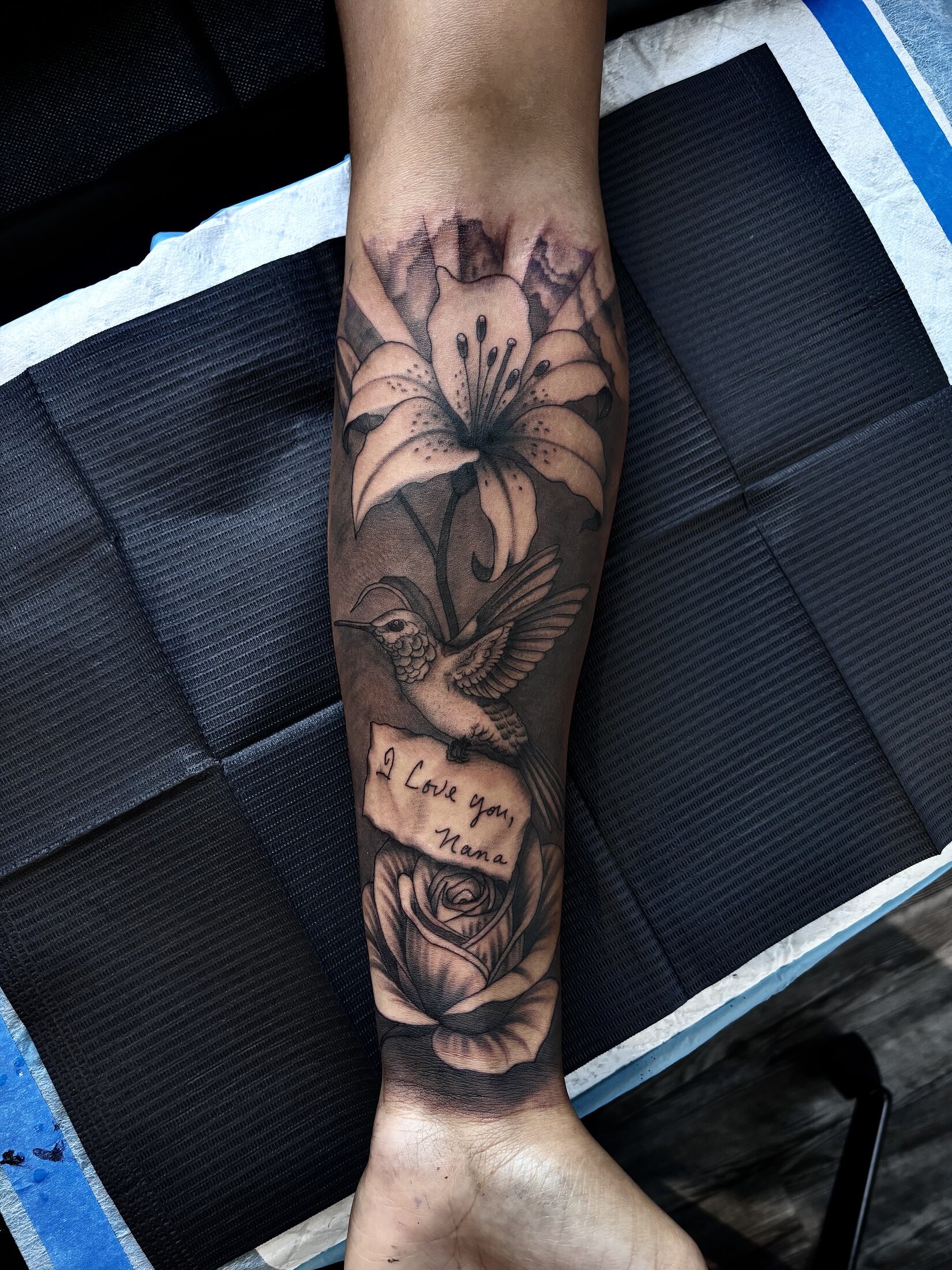 Full black and grey memorial sleeve tattoo of a lily and hummingbird on a forearm