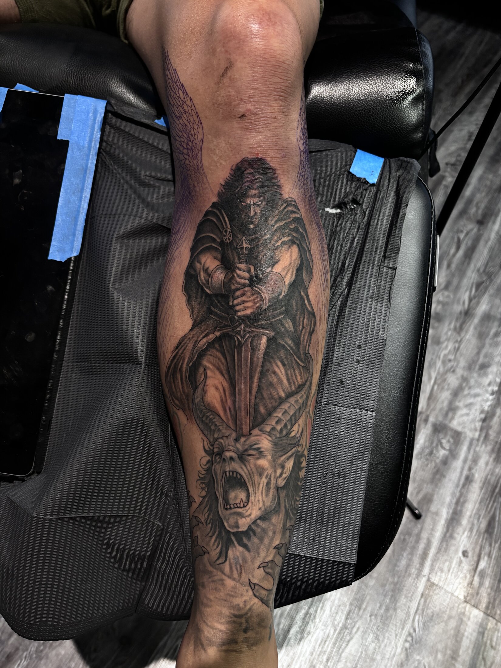 Black and grey realism tattoo of a robed figure with a demonic goat skull on a calf